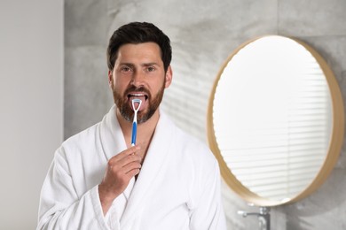 Handsome man brushing his tongue with cleaner in bathroom, space for text