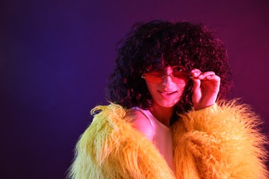 Photo of Beautiful young woman in yellow fur coat and sunglasses on color background in neon lights