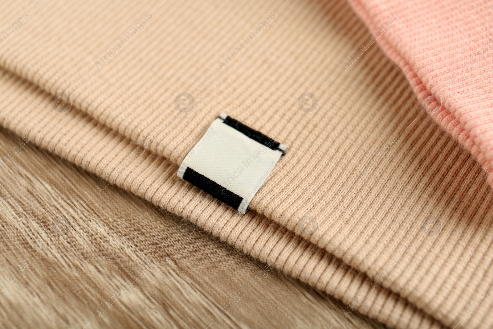 Photo of Beige apparel with blank clothing label on wooden table, closeup