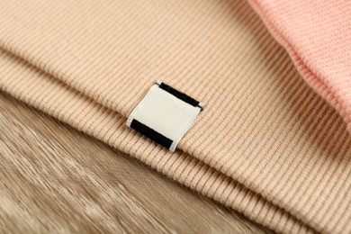 Photo of Beige apparel with blank clothing label on wooden table, closeup
