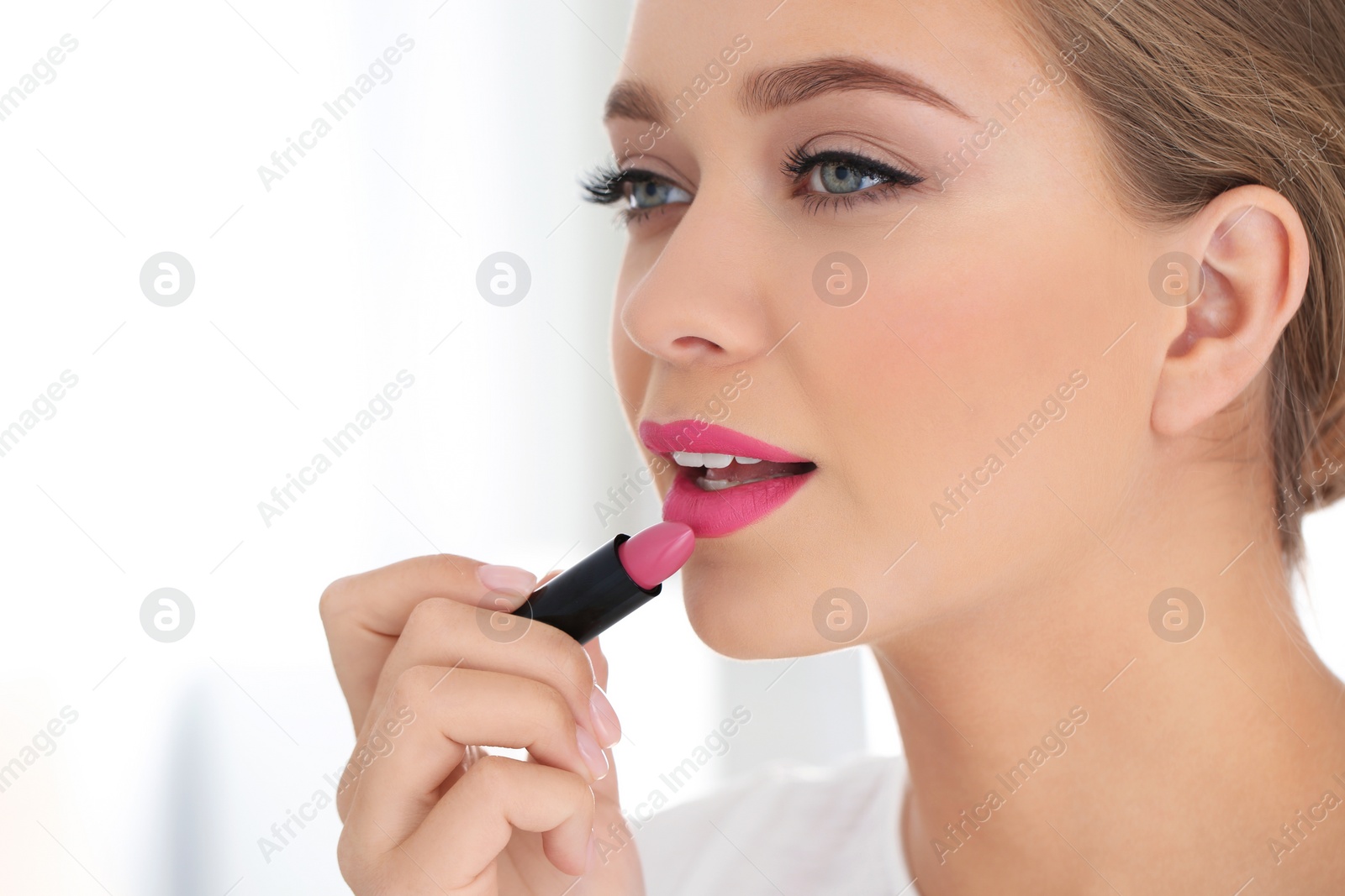 Photo of Beautiful woman applying lipstick on light background