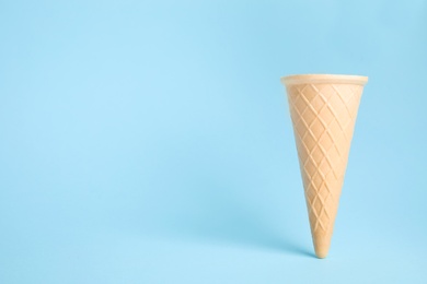 Photo of Empty wafer ice cream cone on blue background. Space for text