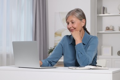 Photo of Beautiful senior woman using laptop at white table indoors
