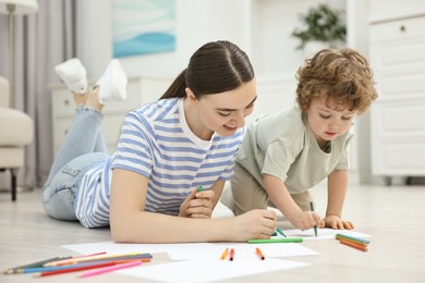 Mother and her little son drawing with colorful markers on floor at home