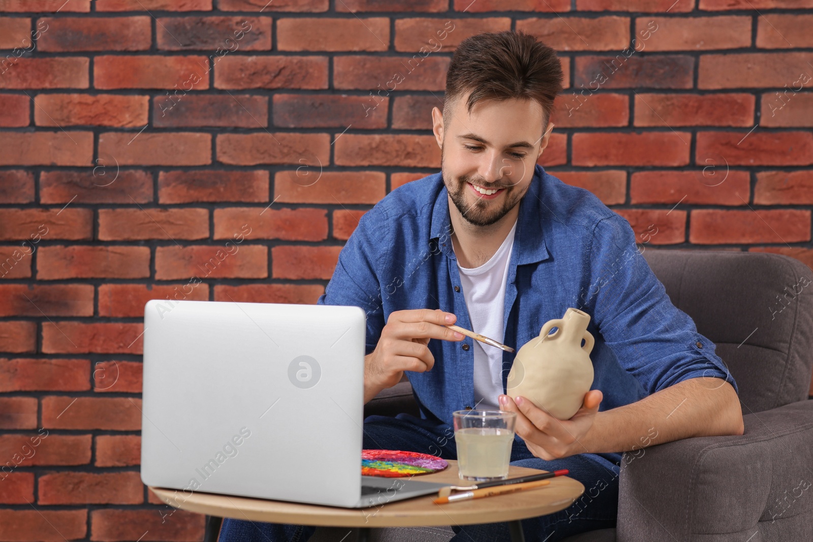 Photo of Happy man learning to decorate clay vase while watching online course at home. Time for hobby