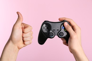 Photo of Man using wireless game controller and showing thumbs up on pink background, closeup