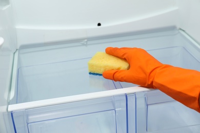 Photo of Worker in rubber gloves cleaning empty refrigerator, closeup