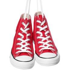 Photo of Pair of new red stylish high top plimsolls hanging on white background