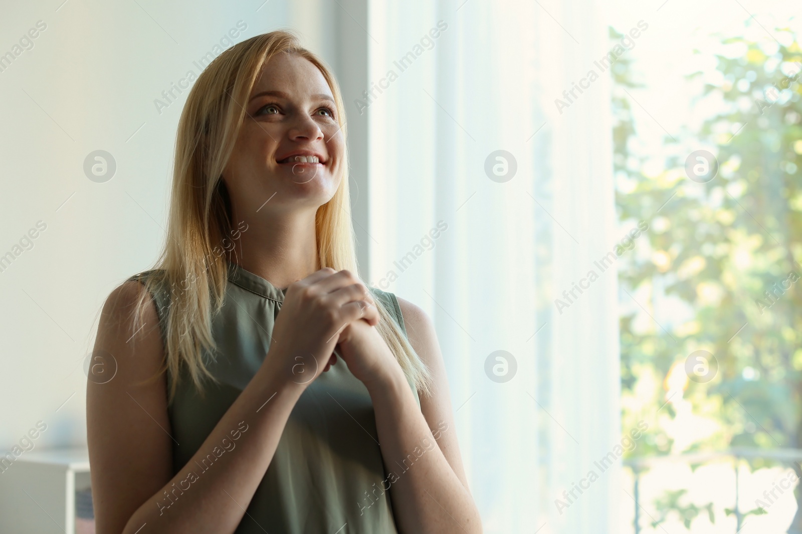 Photo of Religious young woman praying indoors. Space for text