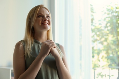 Photo of Religious young woman praying indoors. Space for text