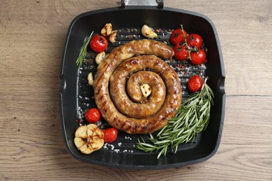 Delicious homemade sausage with garlic, tomatoes, rosemary and spices in grill pan on wooden table, top view