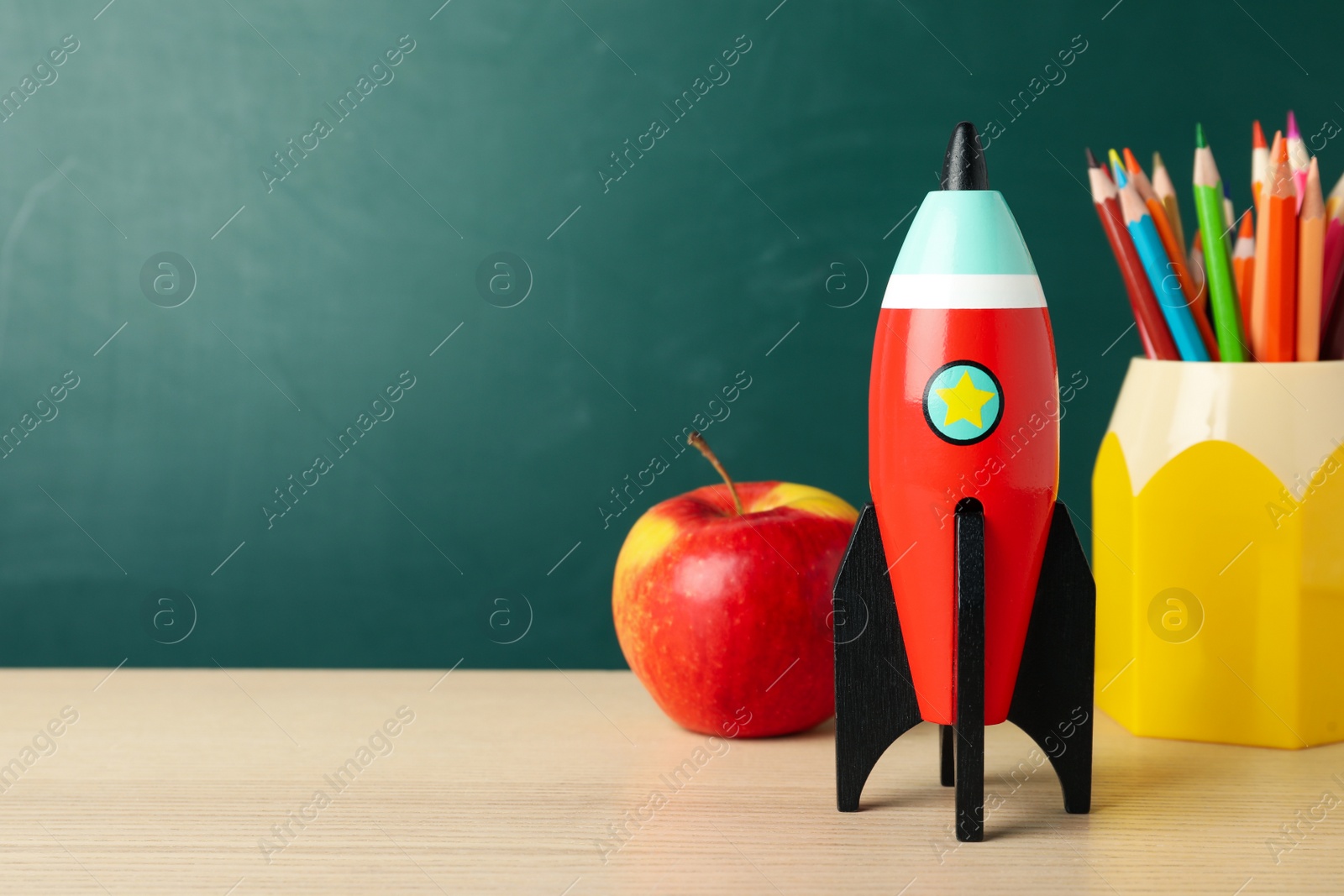 Photo of Bright toy rocket and school supplies on wooden desk. Space for text