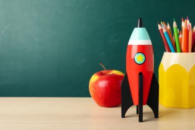 Photo of Bright toy rocket and school supplies on wooden desk. Space for text