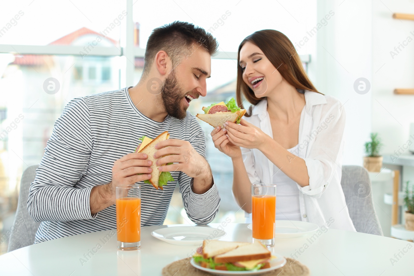 Photo of Happy couple having breakfast with sandwiches at table in kitchen