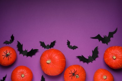 Flat lay composition with black paper bats and pumpkins on purple background, space for text. Halloween celebration