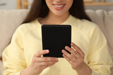 Photo of Young woman using e-book reader indoors, closeup