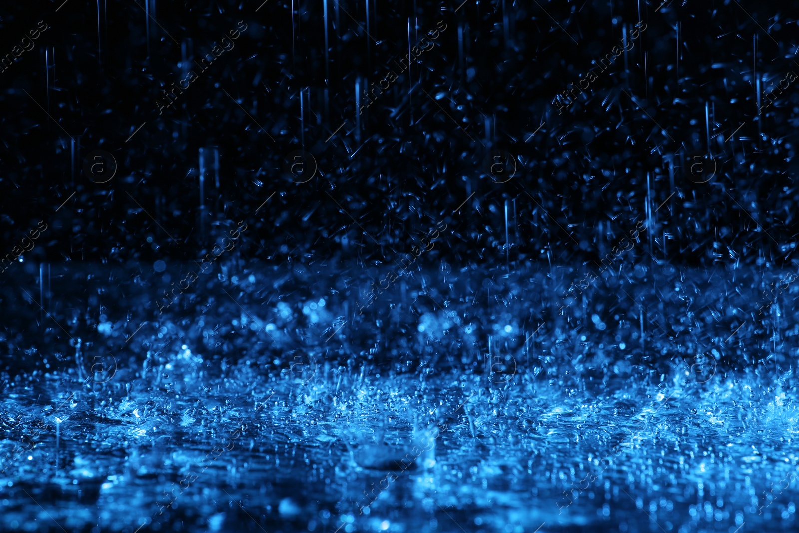 Photo of Heavy rain falling down on ground against dark background, toned in blue