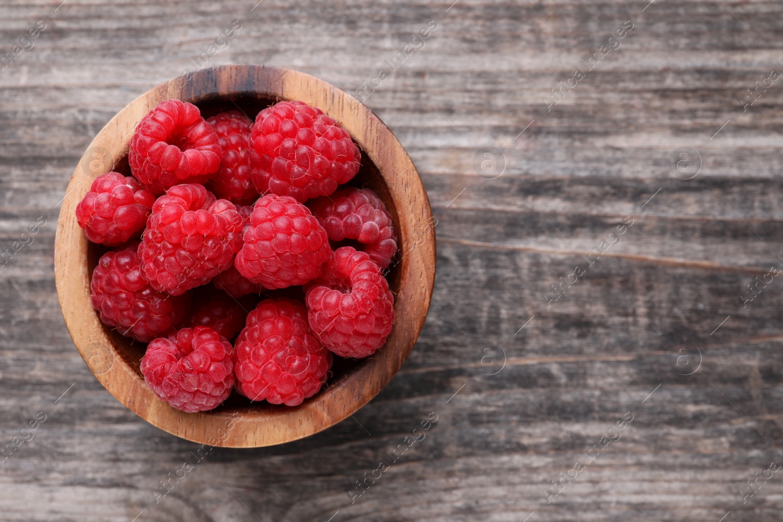 Photo of Tasty ripe raspberries in bowl on wooden table, top view. Space for text