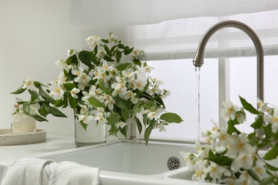 Photo of Bouquet of beautiful jasmine flowers in vase on countertop near kitchen sink