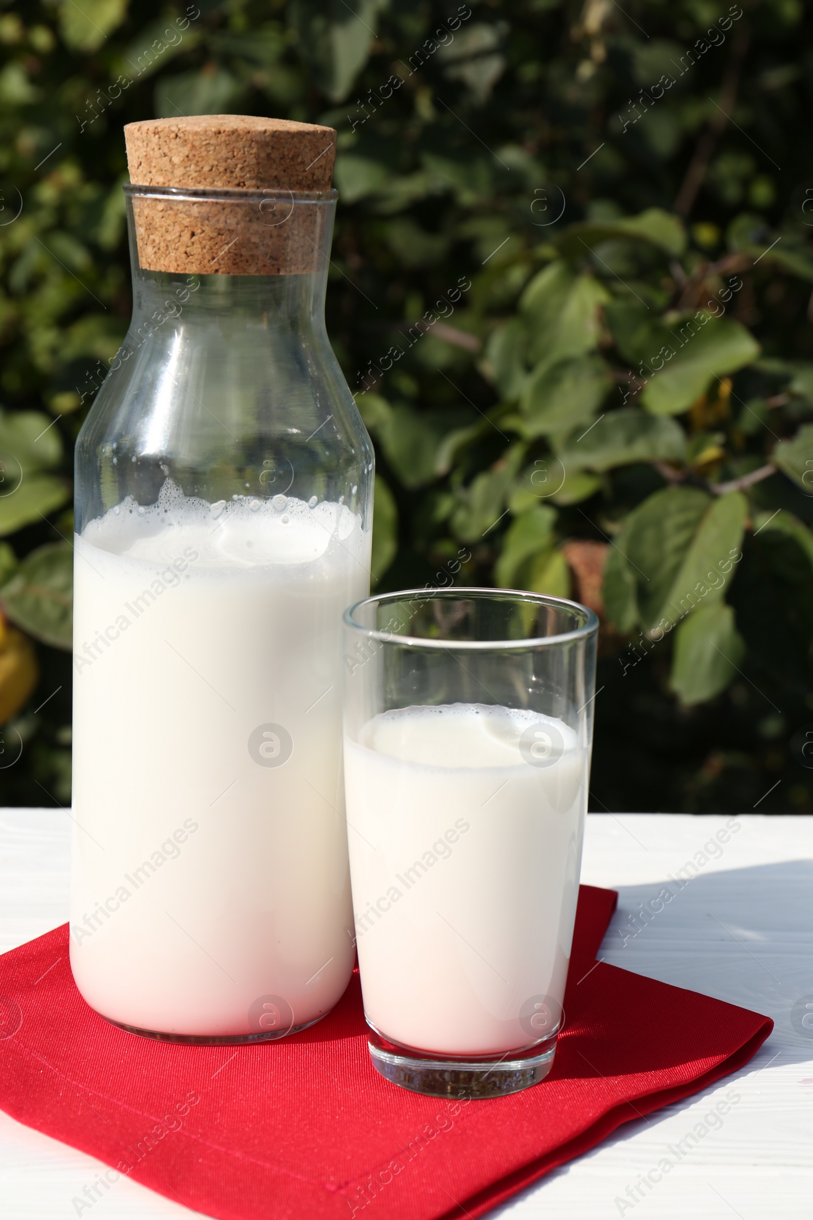 Photo of Glass and bottle of fresh milk on white wooden table outdoors