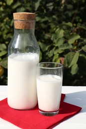 Photo of Glass and bottle of fresh milk on white wooden table outdoors