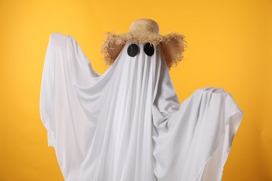Photo of Person in ghost costume and straw hat on yellow background