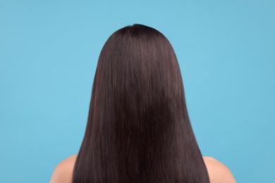 Woman with healthy hair on light blue background, back view