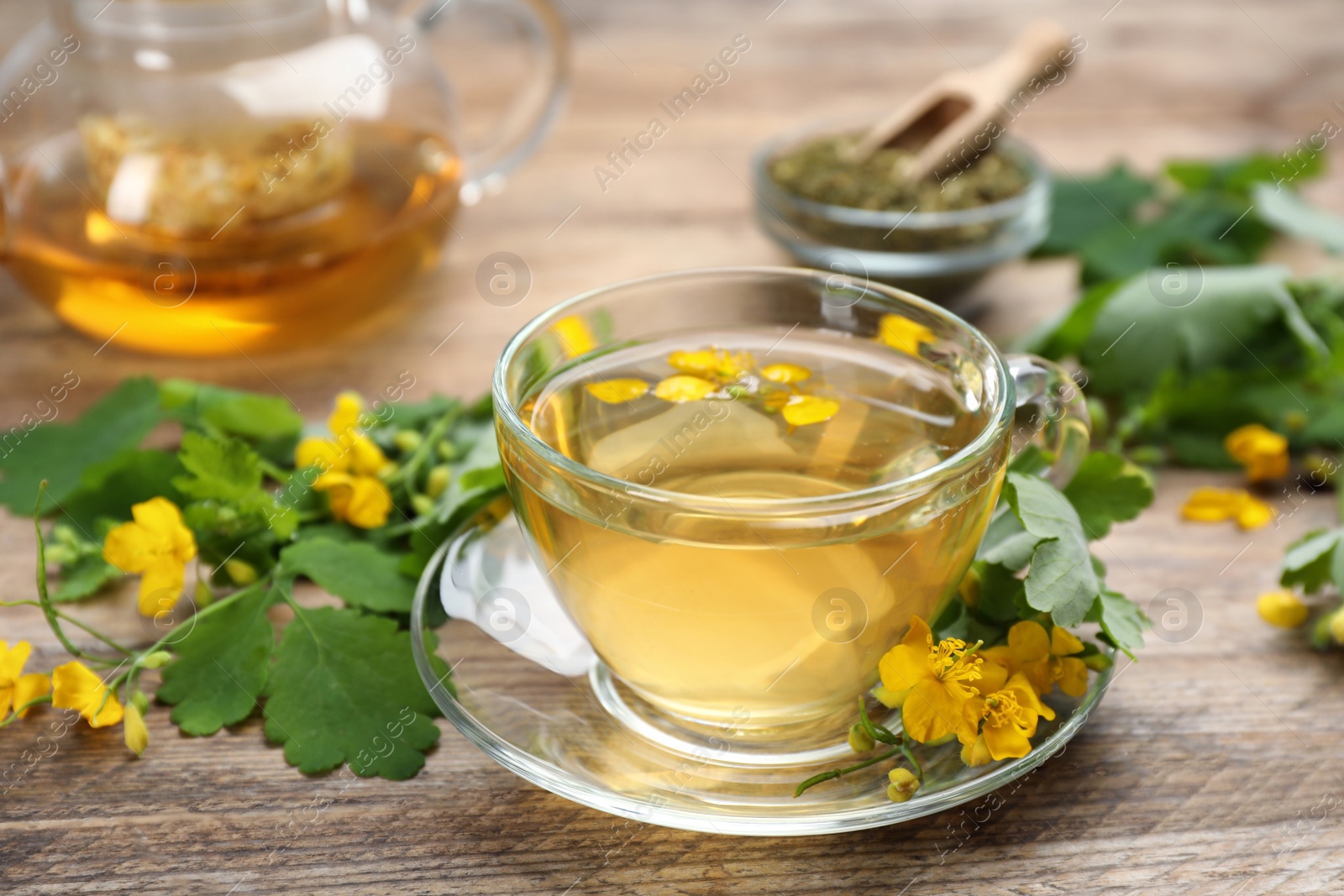 Photo of Glass cup of aromatic celandine tea and flowers on wooden table, closeup