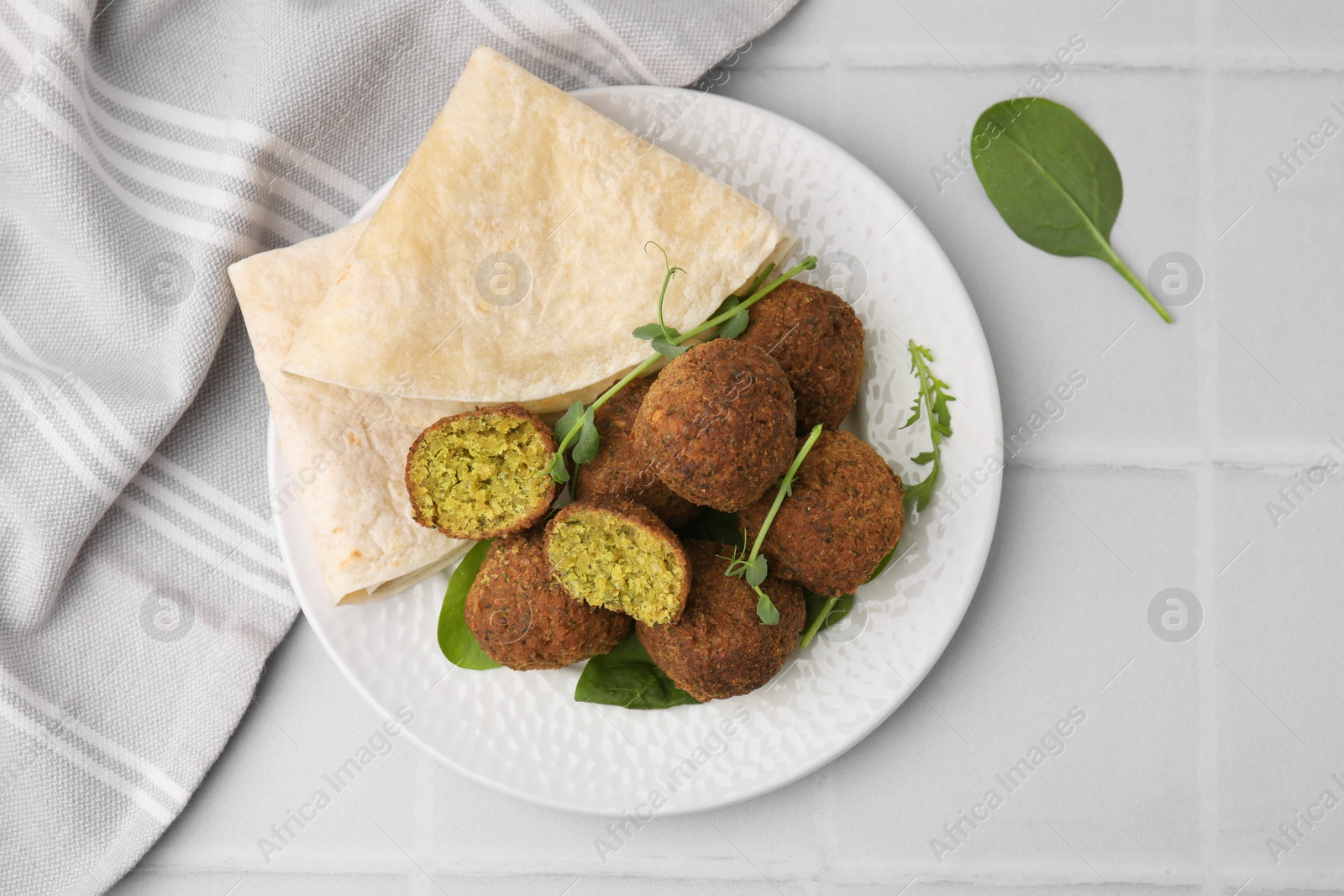 Photo of Delicious falafel balls, herbs and lavash on white tiled table, top view