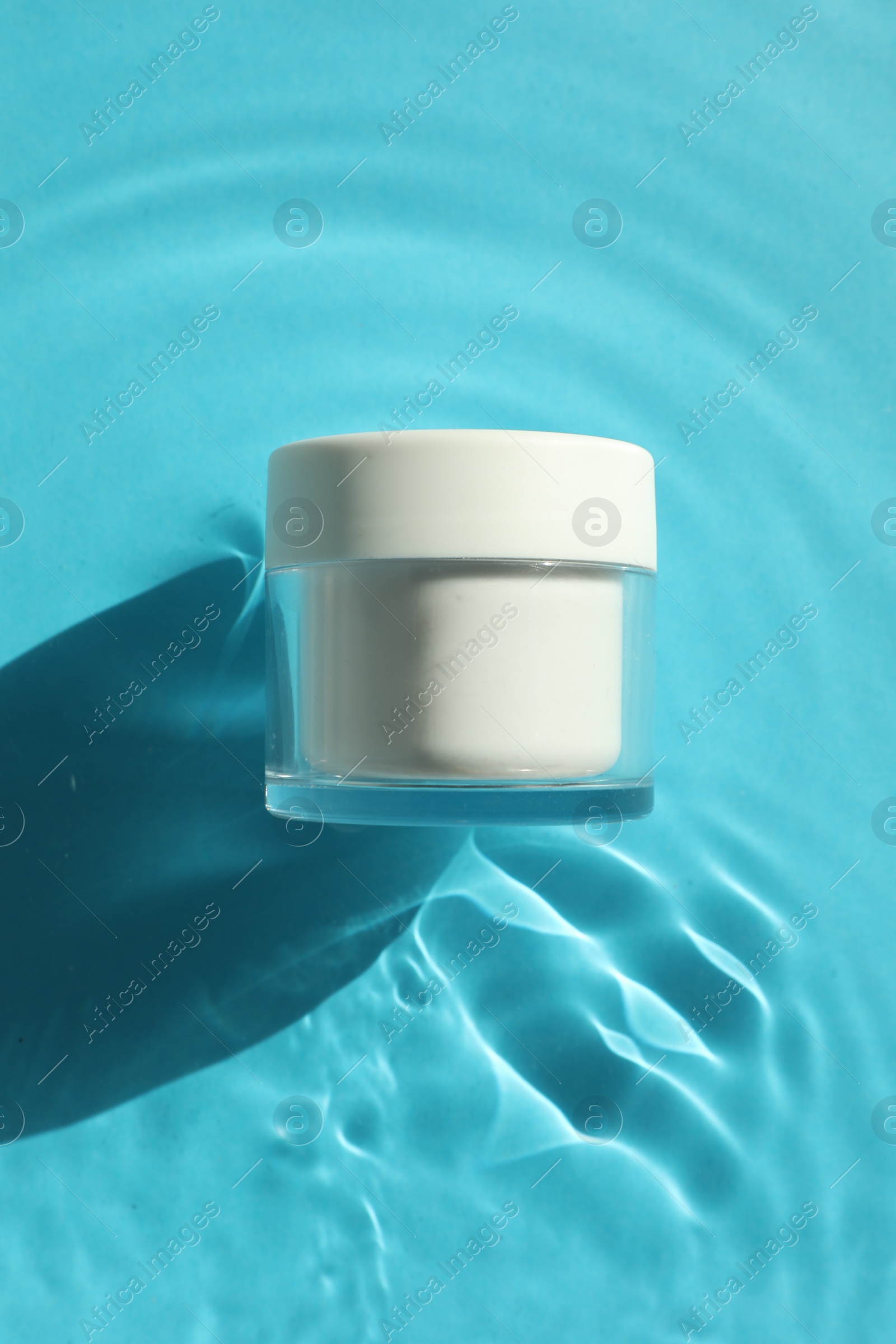 Photo of Jar with moisturizing cream in water on light blue background, top view
