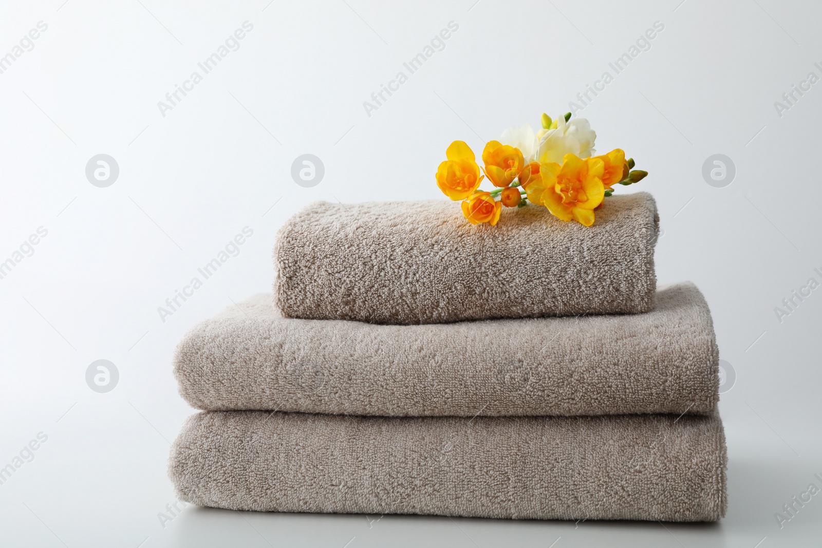 Photo of Stack of fresh towels with flowers on table against white background