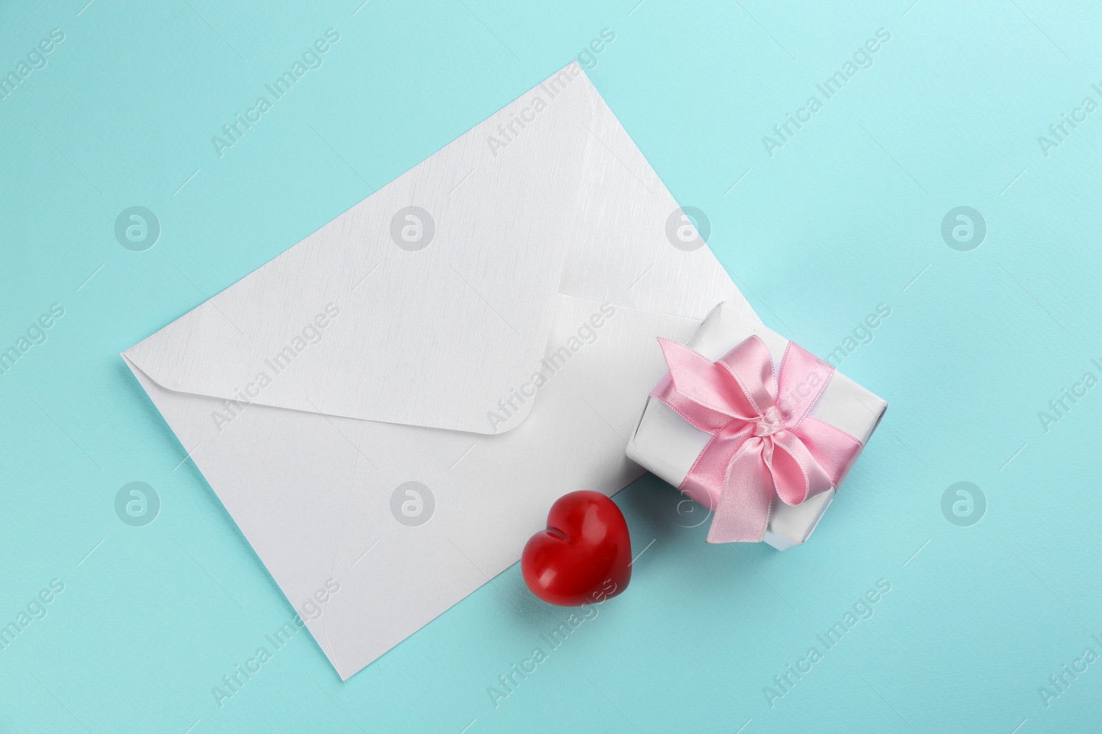 Photo of Beautiful gift box, envelope and red heart on turquoise background, flat lay. Valentine's day celebration