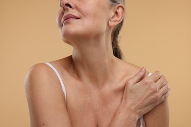 Mature woman with healthy skin on beige background, closeup