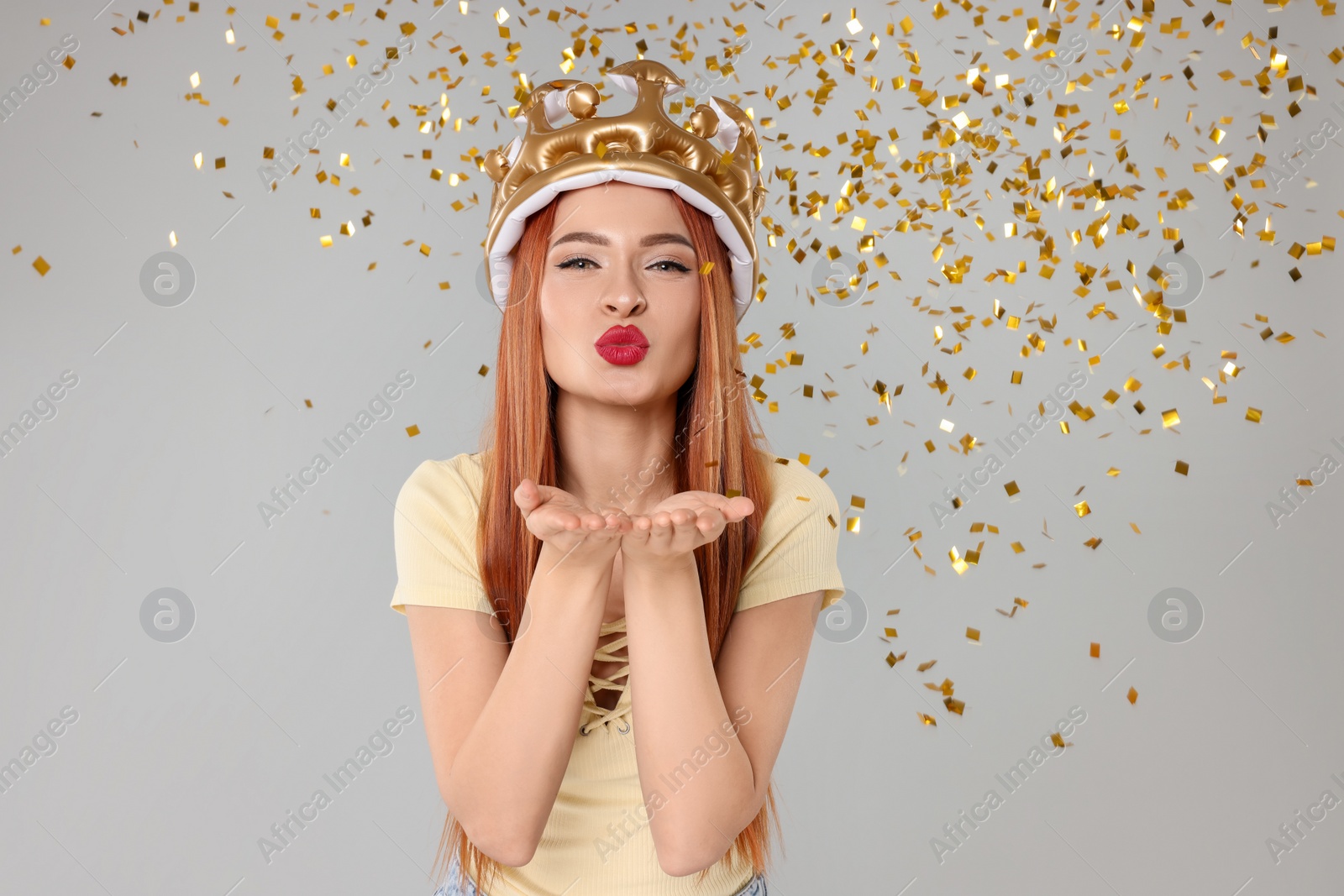 Photo of Beautiful young woman with inflatable crown blowing kiss on light grey background