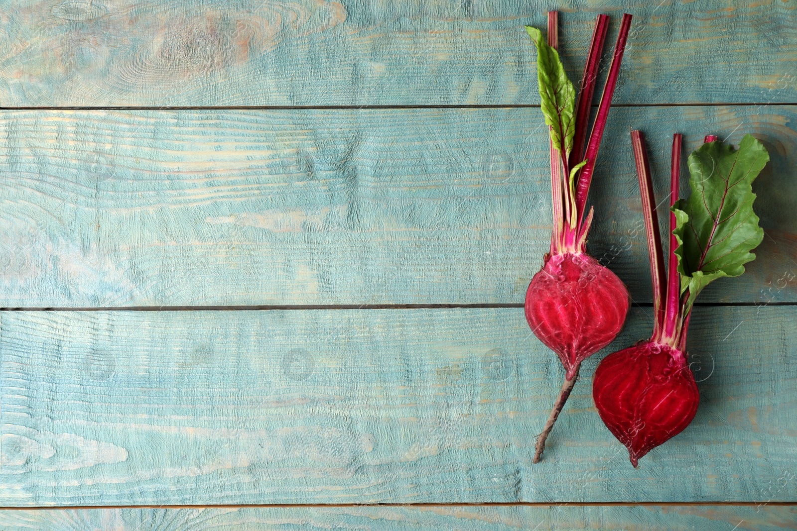 Photo of Halves of raw beet on blue wooden table, flat lay. Space for text