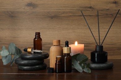 Aromatherapy products and burning candle on wooden table