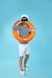 Photo of Sailor with orange ring buoy looking through binoculars on light blue background