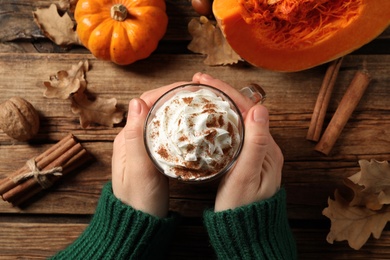 Photo of Woman holding tasty pumpkin latte at wooden table, top view