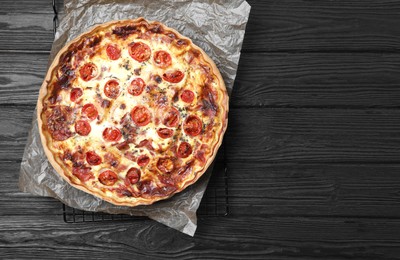 Delicious homemade quiche with prosciutto and tomatoes on black wooden table, top view. Space for text