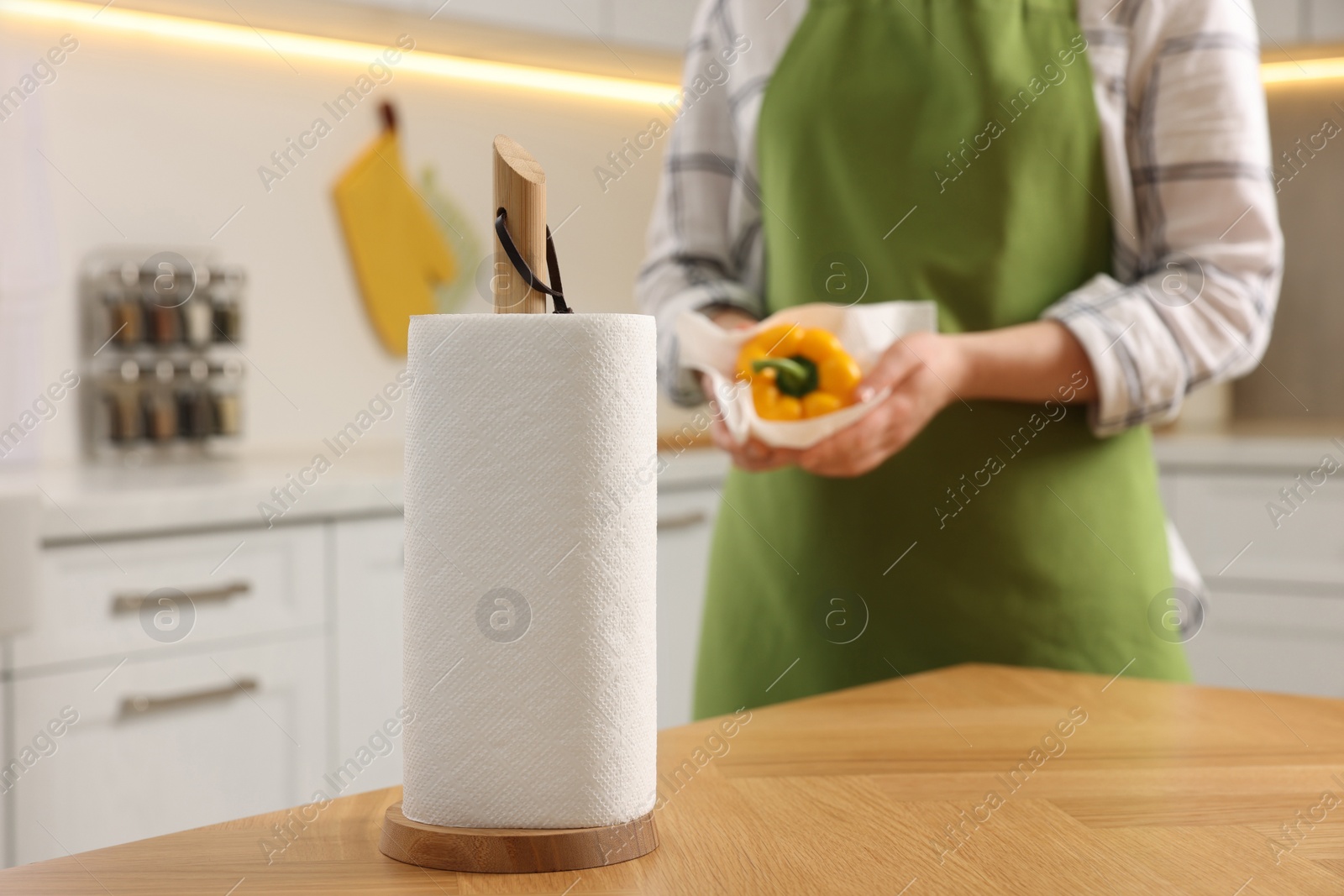 Photo of Roll of paper towels in kitchen and woman wiping bell pepper on background. Space for text