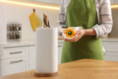 Roll of paper towels in kitchen and woman wiping bell pepper on background. Space for text