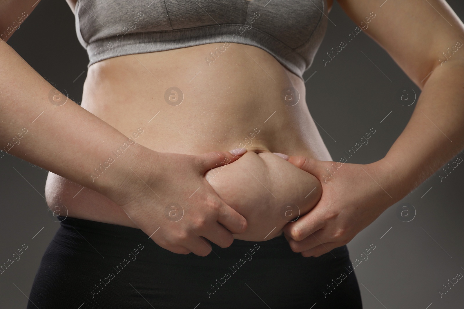 Photo of Woman touching belly fat on grey background, closeup. Overweight problem