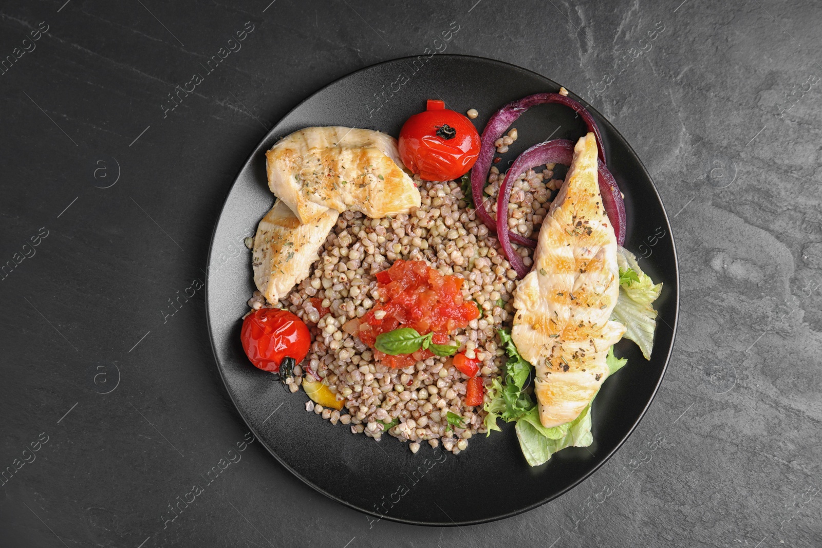 Photo of Tasty buckwheat porridge with meat and vegetables on dark grey table, top view