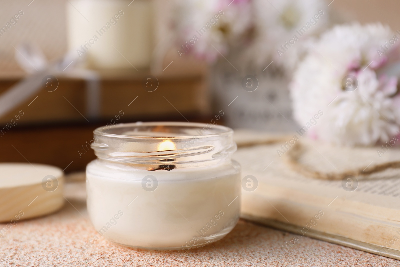 Photo of Burning candle and book on beige textured table
