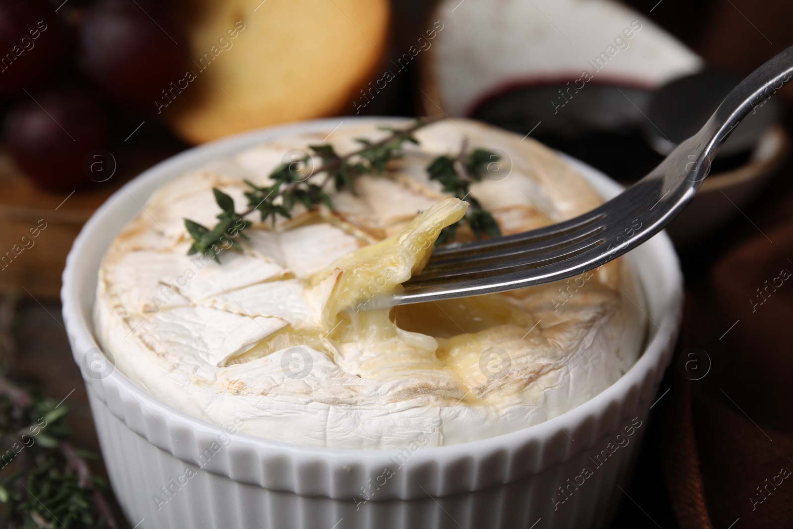 Photo of Eating tasty baked camembert with fork from bowl at table, closeup