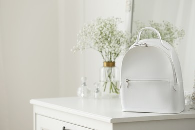 Photo of Stylish white backpack on chest of drawers indoors, space for text