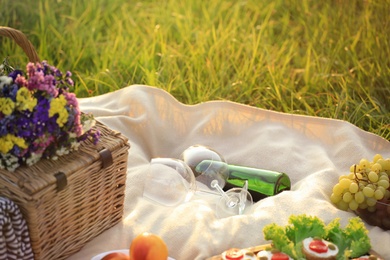 Photo of Blanket with picnic basket and wine on green grass