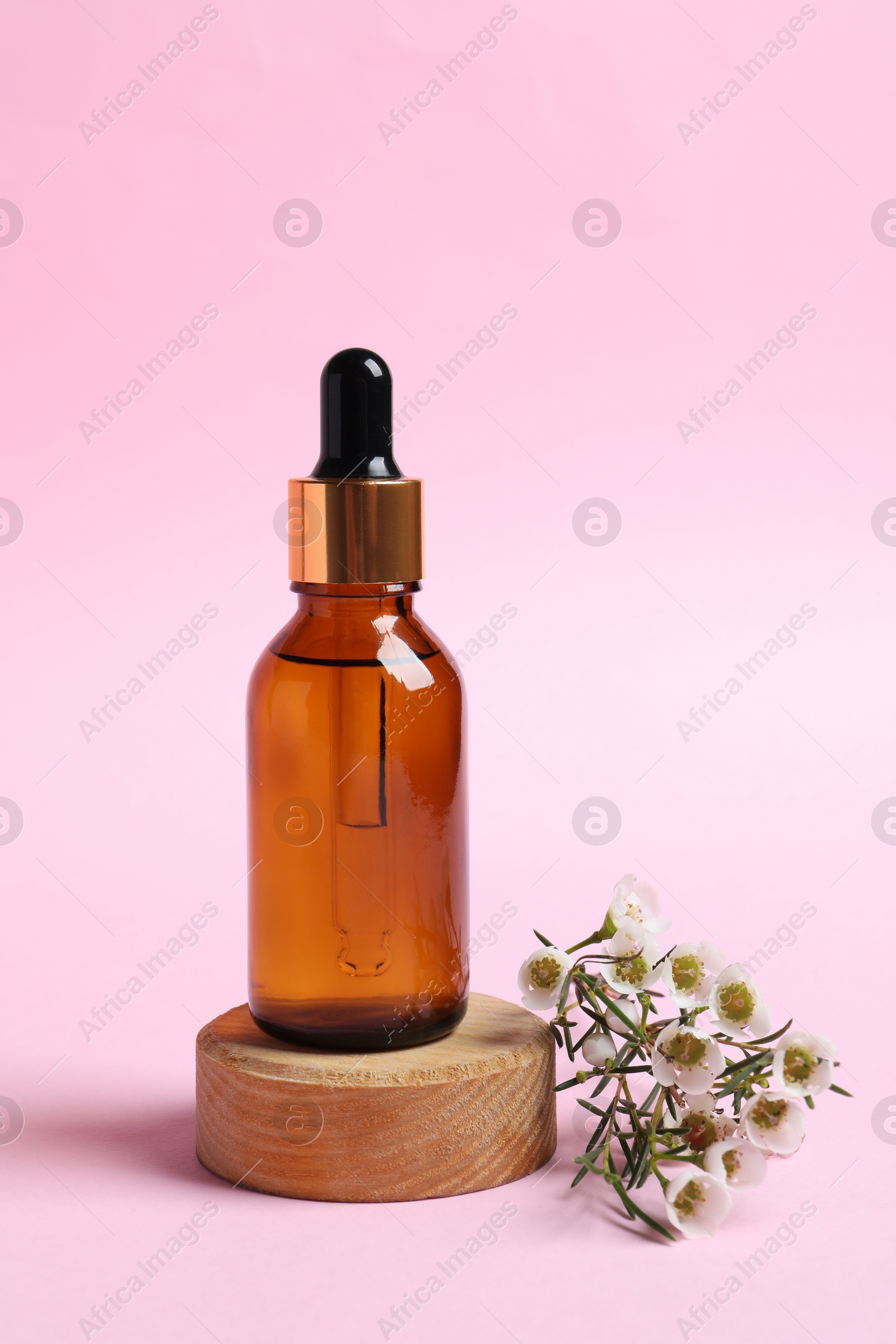 Photo of Bottle with cosmetic oil and flowers on pink background