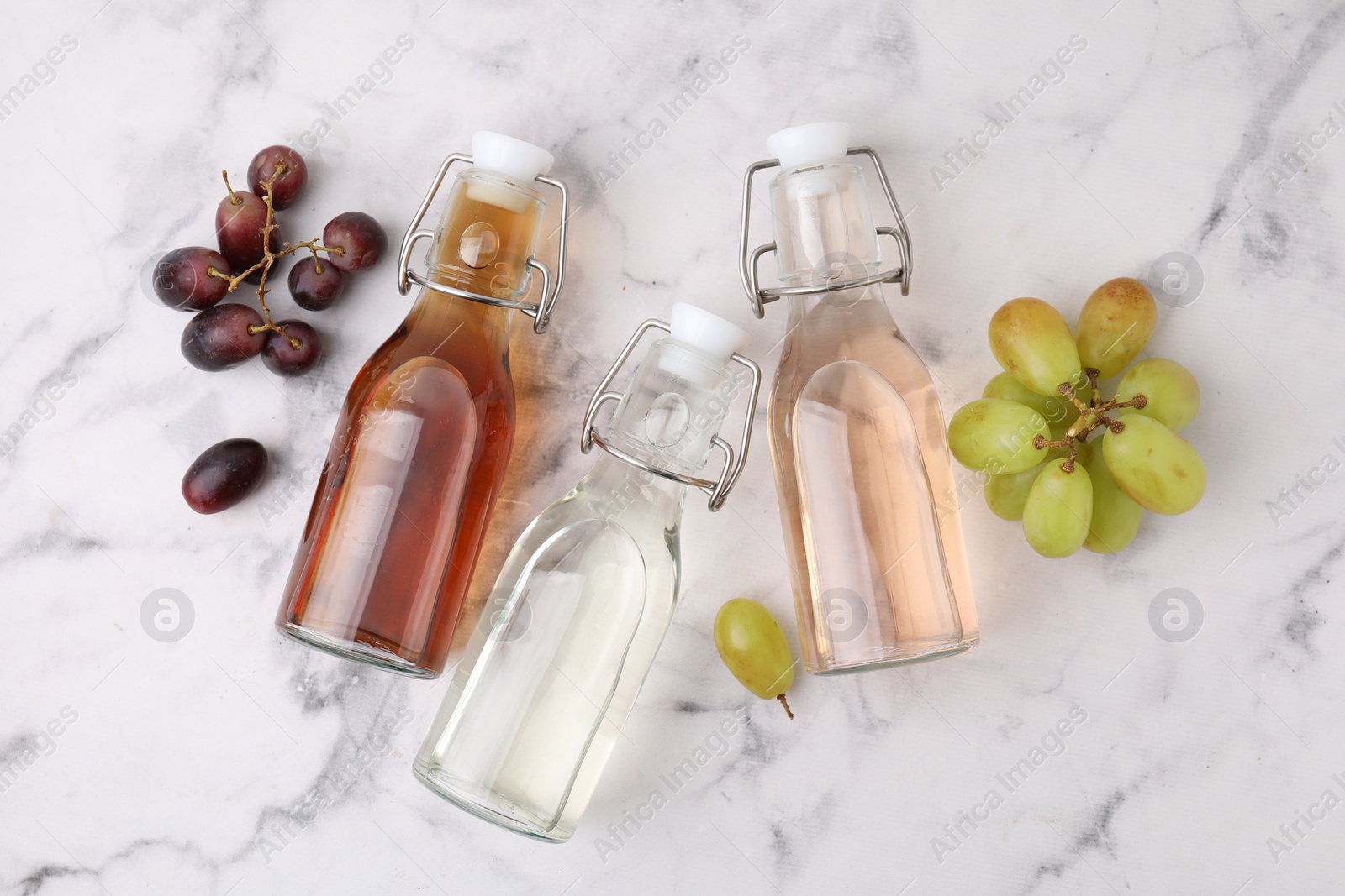 Photo of Different types of vinegar in bottles and grapes on light marble table, flat lay