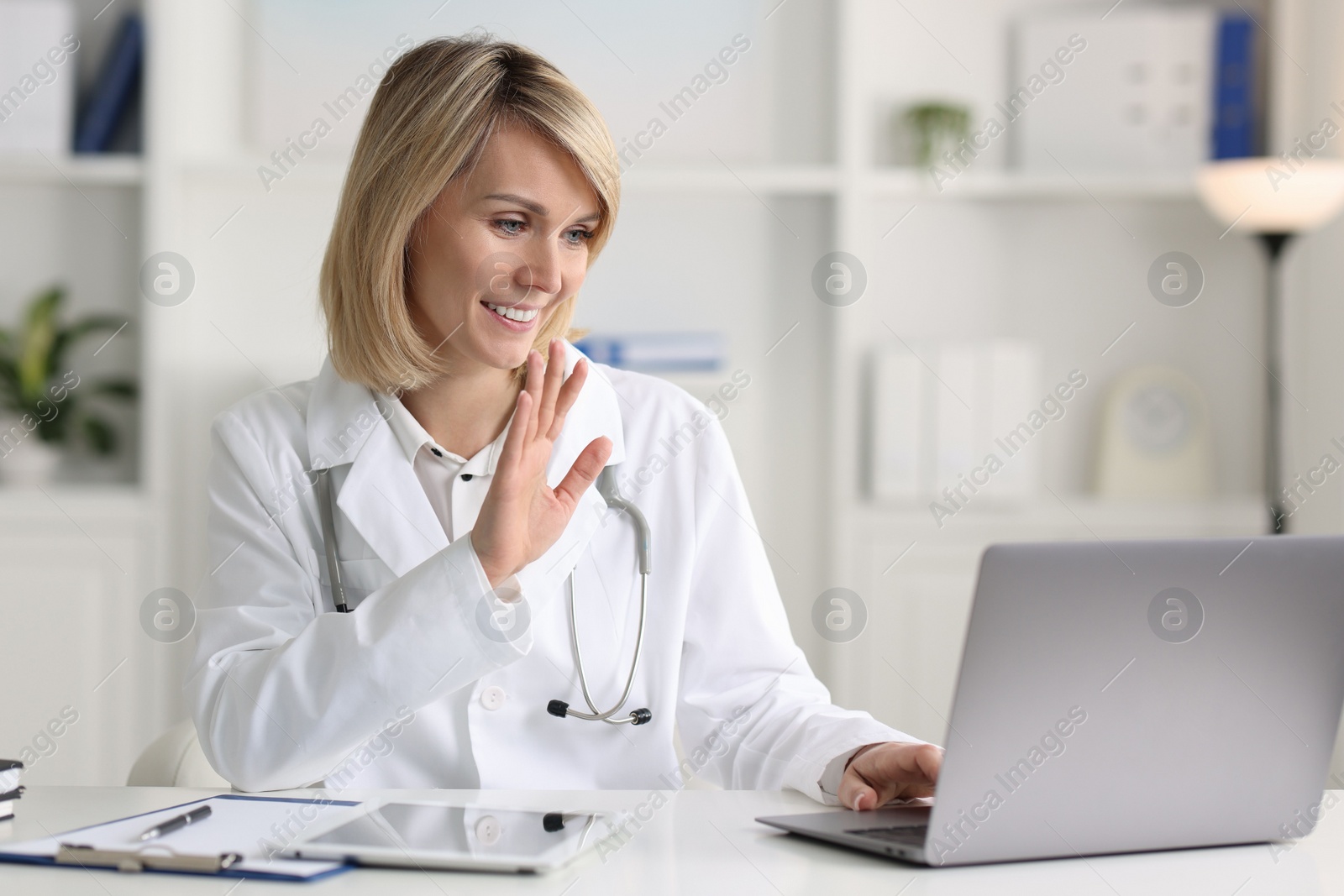 Photo of Smiling doctor with laptop having online consultation at table in office